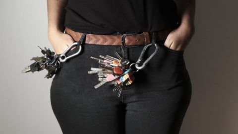 תמונה של חלק אמצעי של גוף אישה, לבושה בחולצה שחורה, מכנסי ג'ינס שחורות ולמכנסיים מחוברים מספר צרורי מפתחות גדולים
